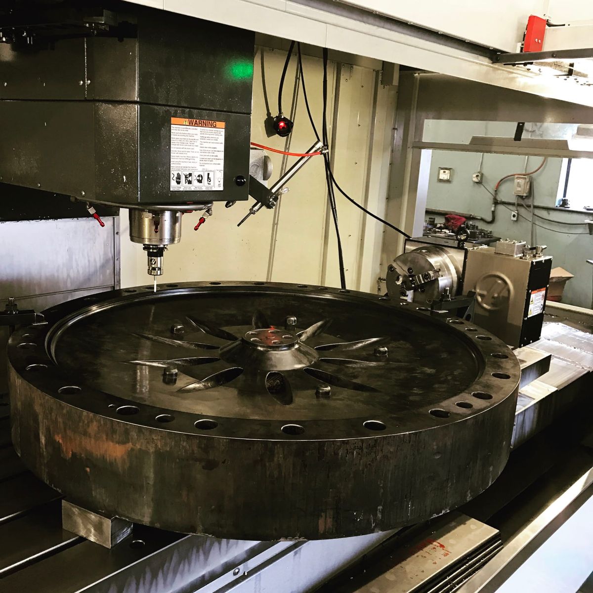 Large round part on a CNC mill table with a 4th-axis rotary beside it