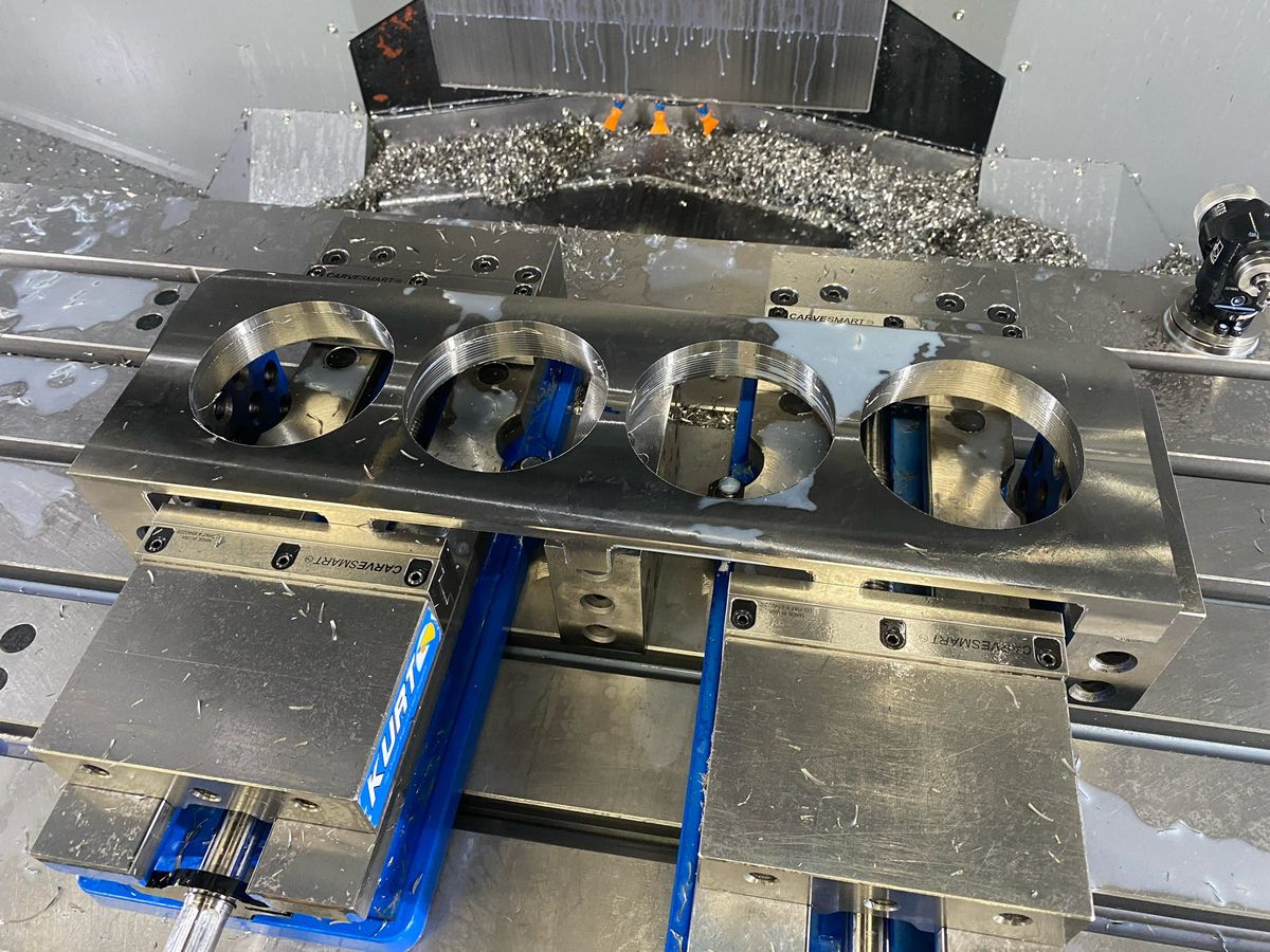 Four-bore plate held in two vises inside a CNC machining center